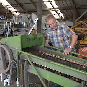 In de open schuur staat een kleine sorteermachine die handmatig werkt. Zodra Bakker aan het grote wiel draait, begint de machine te schudden en worden de aardappelen in drie maten gesorteerd.