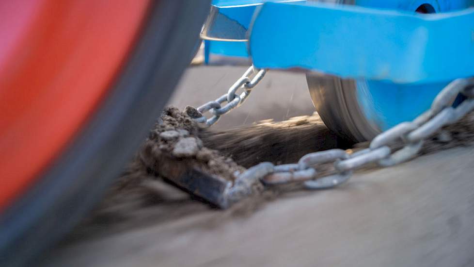 Na deze rol een ijzeren stripje met lichte V-vorm, gehangen aan 2 kettinkjes. Deze dekken het zaad weer toe. Links in beeld is de brede aandrukrol te zien, welke de rug weer netjes verdicht.